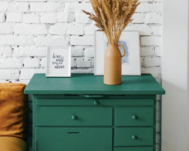 a green dresser with a vase of dried flowers on top of it